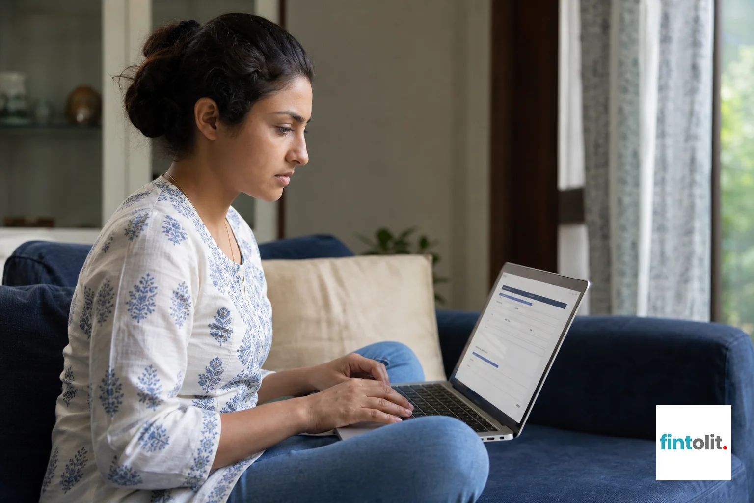 Person filing an online complaint on a laptop. Photorealistic photo of an Indian woman in her late 20s sitting on a sofa at home, typing on a laptop with a government-style complaint form visible on screen, focused and determined