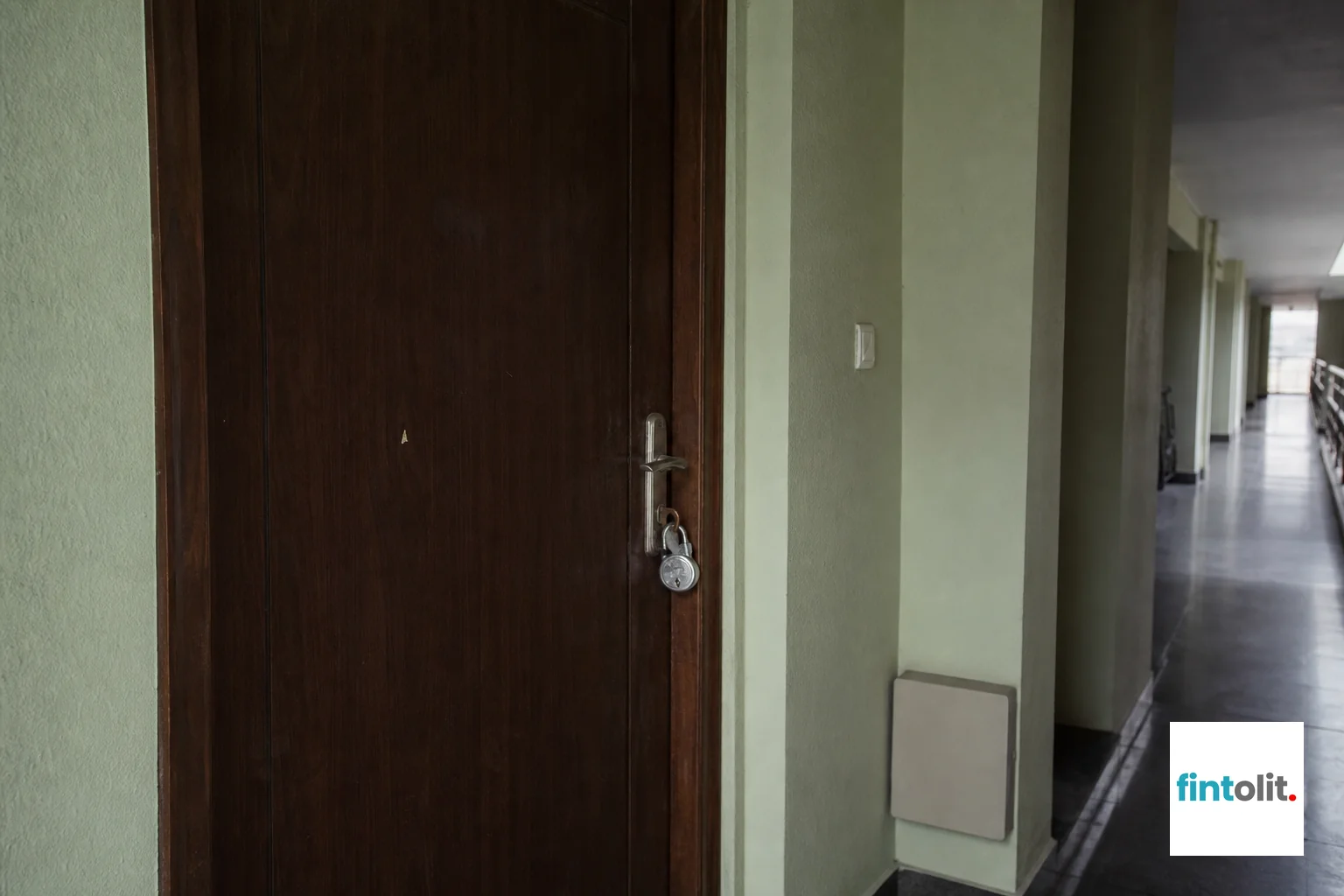 A locked apartment door with a padlock, symbolizing illegal lockout attempts. Photorealistic photo of a residential apartment front door in an Indian housing complex with a padlock attached to the door handle, dim hallway lighting, muted