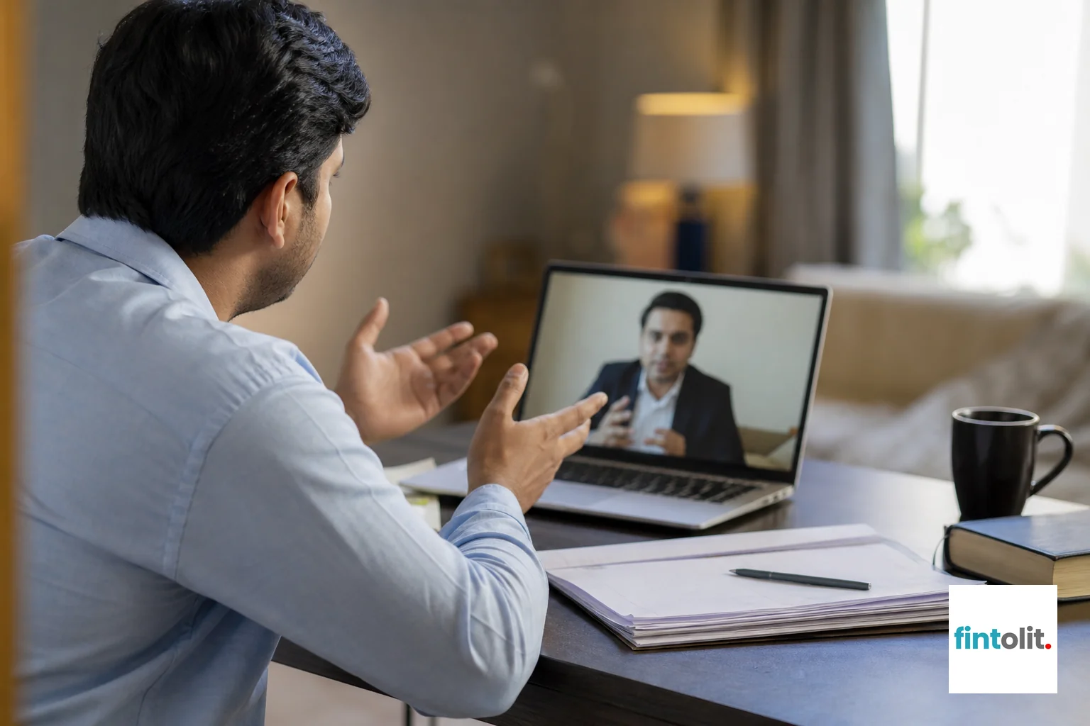 Photograph a person of Indian appearance sitting in a video call at home, laptop screen visible but not readable, with notes or documents on the desk beside them. Capture the moment of active listening or note-taking. Soft, natural