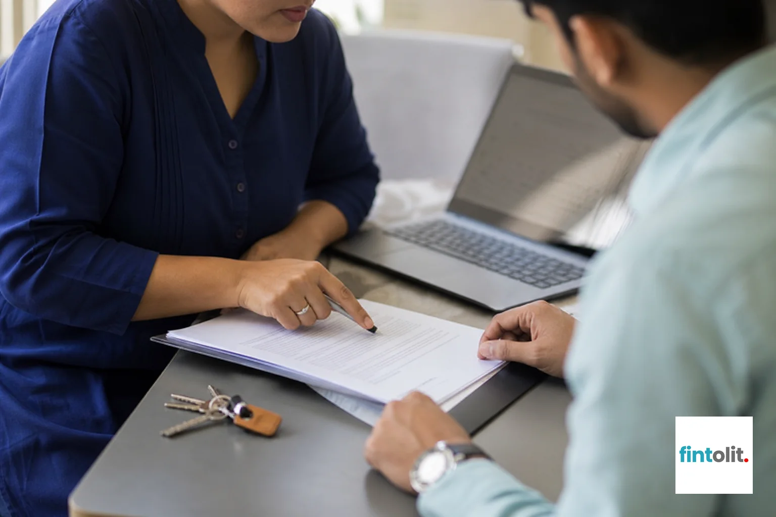 Property documents and keys being reviewed for post-divorce title transfer in Delhi NCR. Natural close-up photography of people of Indian appearance concentrating on an everyday professional moment, laptops or notes nearby with screens